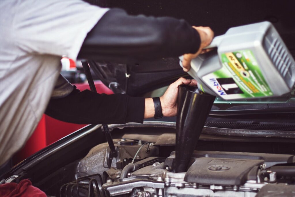 an auto technician pours mobil 1 synthetic motor oil into a car's engine